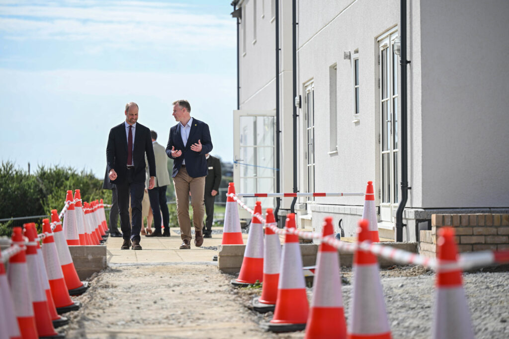 Duke Of Cornwall There Are Two Men Walking Down A Sidewalk Between Orange And White Cones